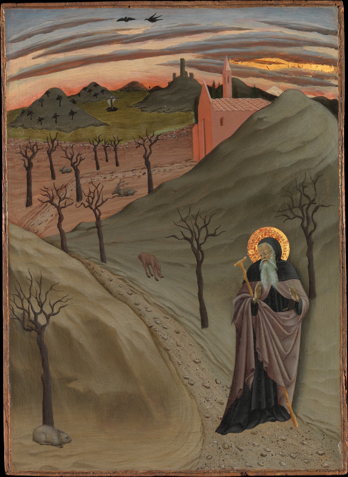 Sano di Pietro’s white-bearded Anthony with a gold halo and staff, walking alone through a bare hillside wilderness.