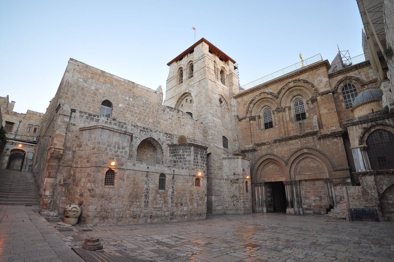 The stone entrance front of the Church of the Holy Sepulchre, with twin arched doorways and a bell tower, above a paved courtyard.