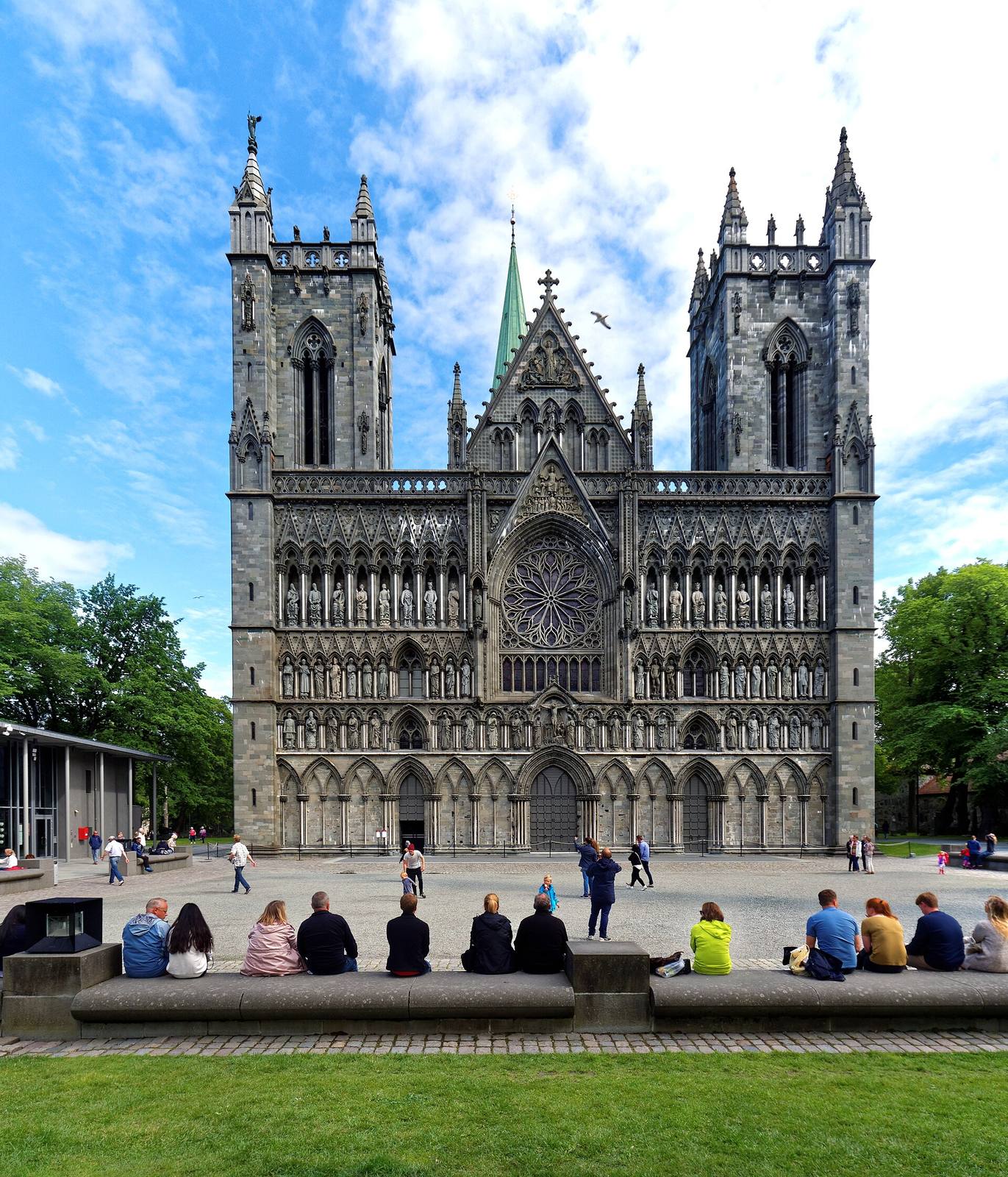 The sculpted west front of Nidaros Cathedral with its rose window, with people in front.