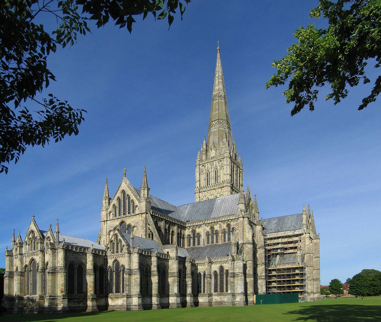 Salisbury Cathedral and its tall spire in early morning light, across a lawn.