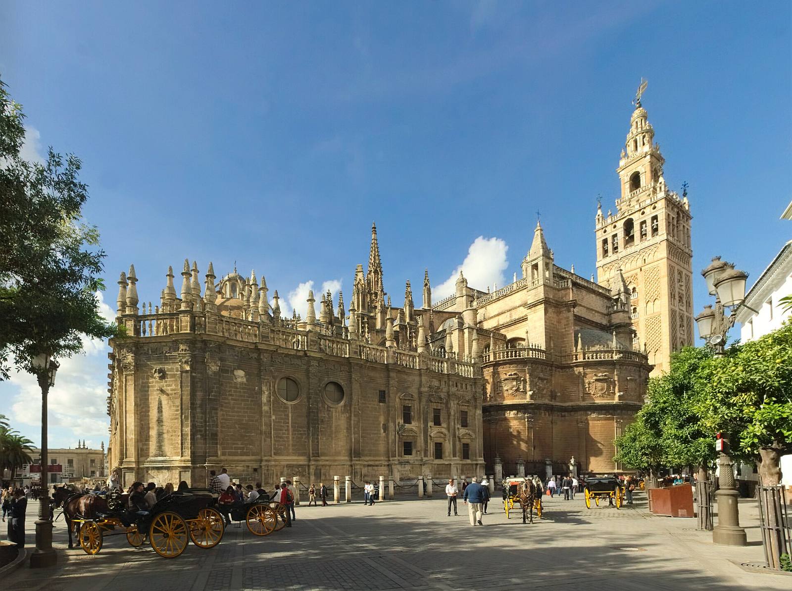 Seville Cathedral’s Gothic south-east side and the Giralda bell tower, with horse carriages in the square.